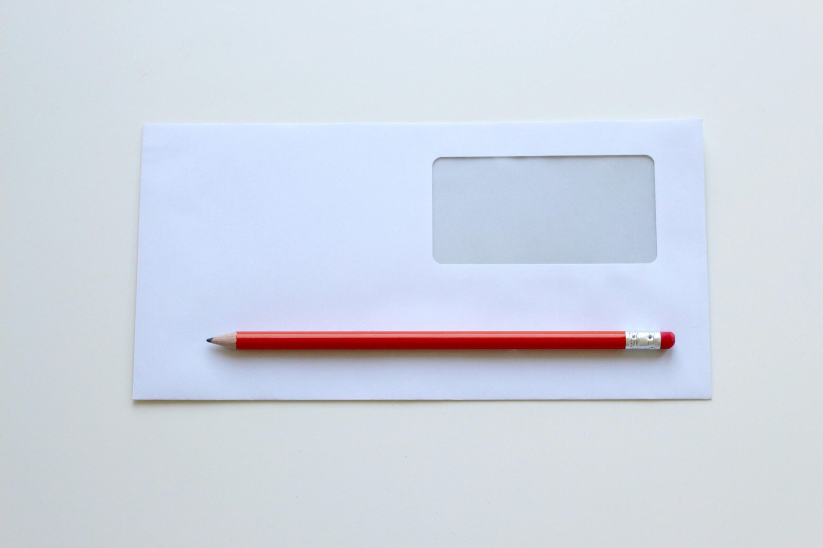 Minimalist photo of a red pencil on a blank white envelope with window. Perfect for stationery themes.